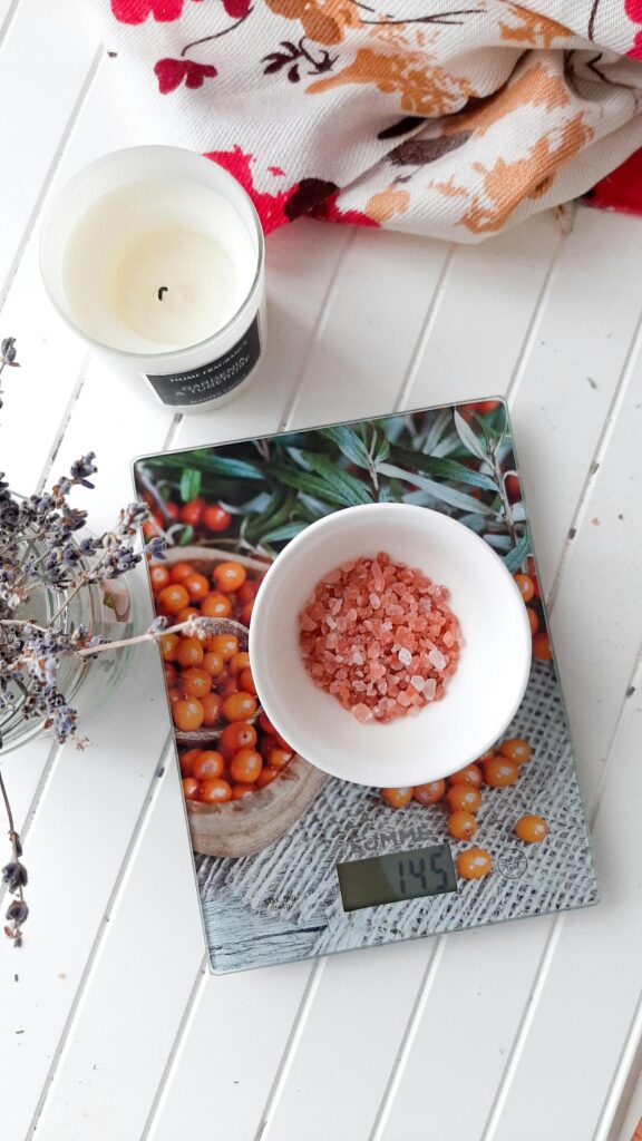 Top view of pink Himalayan salt in a bowl on a decorative digital scale with a candle nearby.