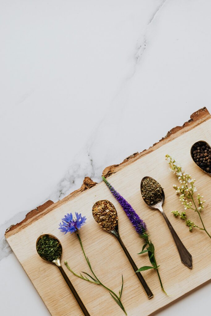 Close-up of various herbs and flowers in spoons on a wooden board, perfect for natural remedies.