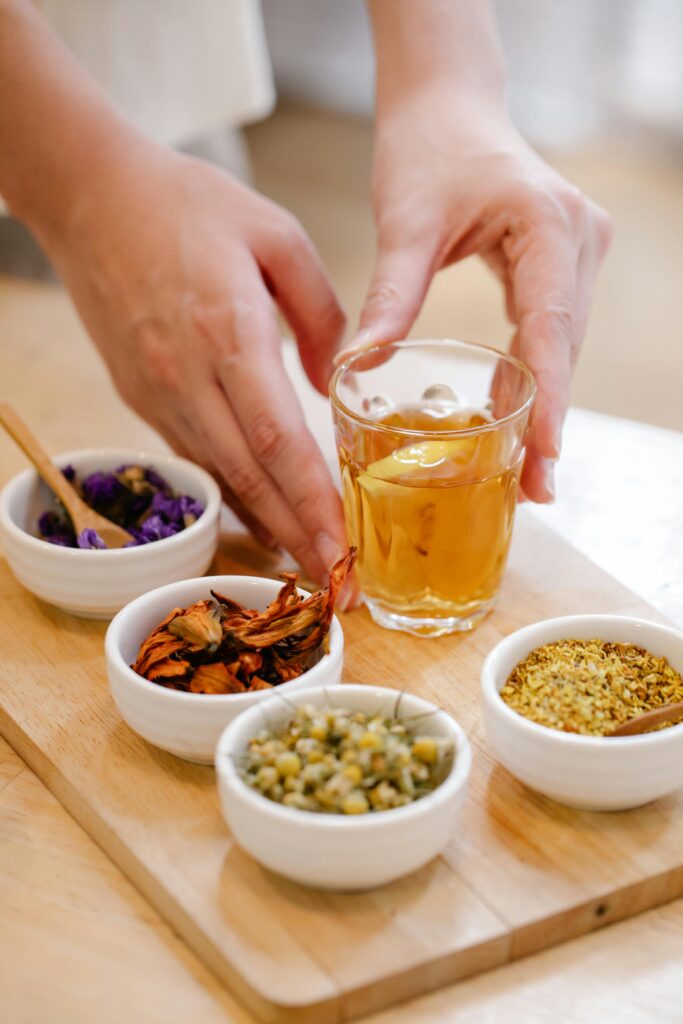 Person arranging herbal tea with various herbs on wooden board.